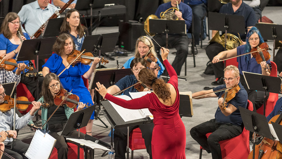 A woman in red dress passionately conducts a symphony.