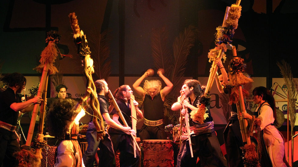 An orchestra performs on stage with indigenous instruments.