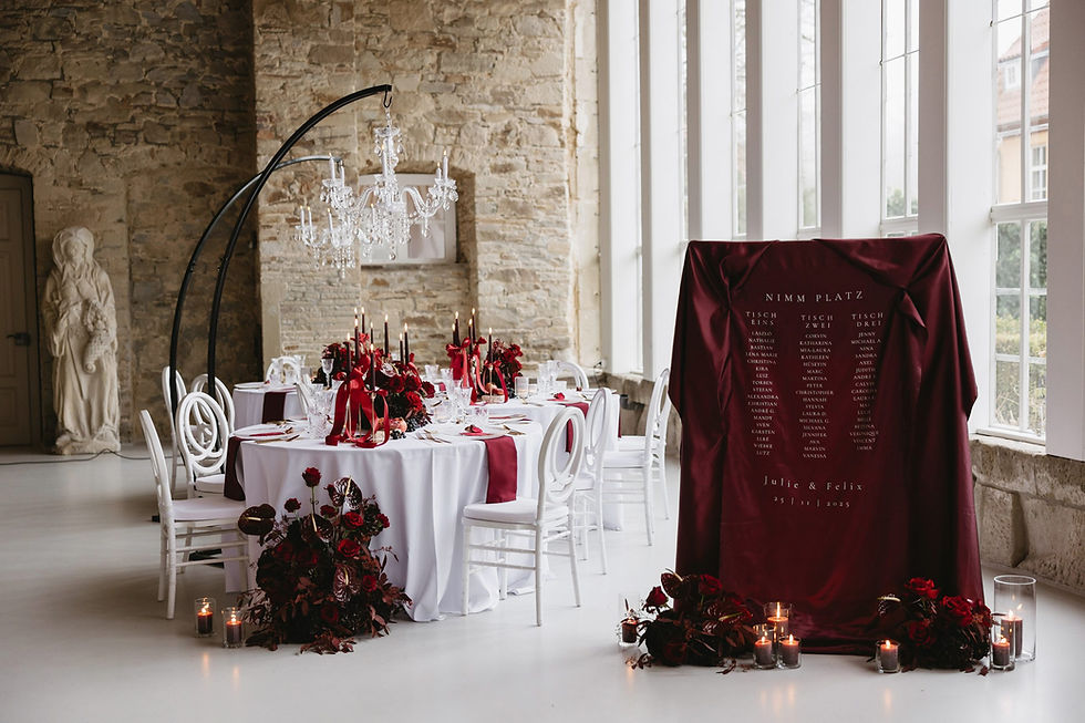 Hochzeitstafel mit roter Floristik, schwarzen Kerzen, Satinbändern und Sitzplan in der Orangerie Gut Ostenwalde bei Osnabrück