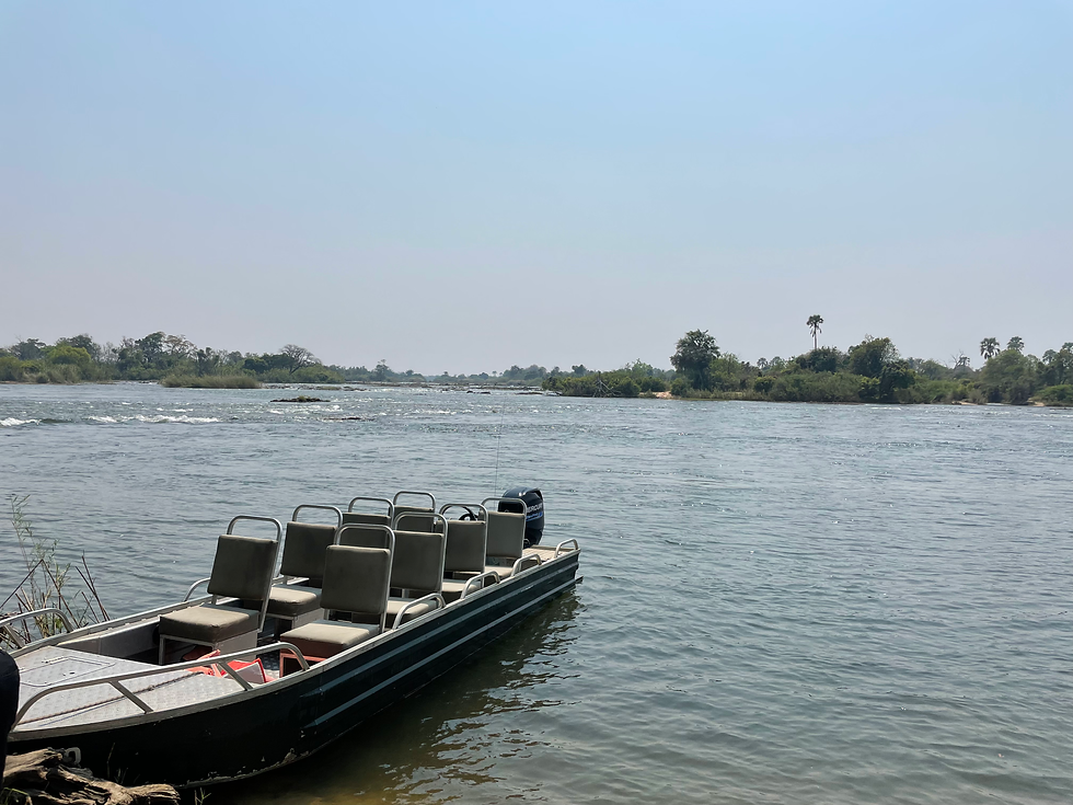 Boat crossing Zambezi River toward Livingstone Island with Victoria Falls spray visible