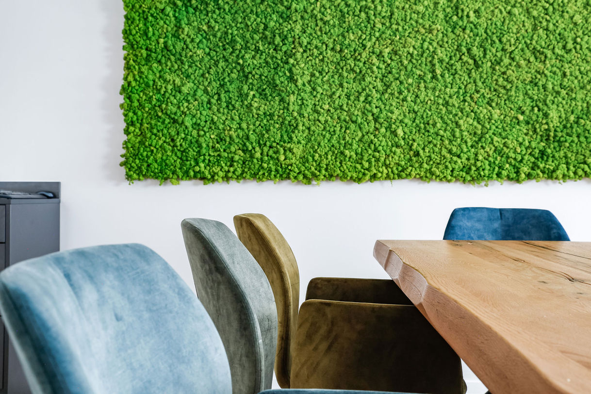 Besprechungsraum der Bodensteiner Gruppe mit einem großen Holztisch in der Mitte, umgeben von mehreren bunten Stühlen. An der Wand ist Moos dekoriert, und im rechten Bildrand ist ein Teil eines Kickers zu sehen.