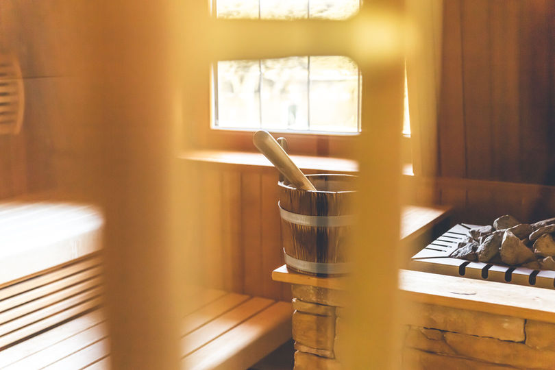Blick in die Finnische Sauna im Wellnessbereich des Hotels Deutschherrenhof: Auf der Kante des Saunaofens steht ein Holzkübel mit einer Kelle.