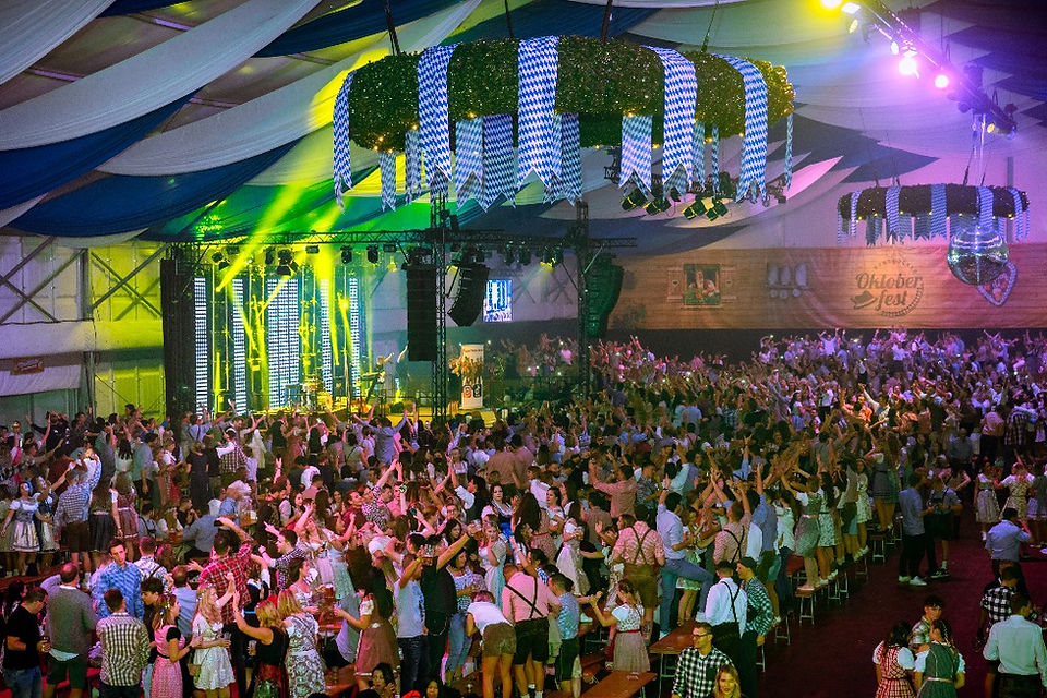Ein voll besetztes Festzelt beim Hunsrücker Oktoberfest: Unzählige Menschen in Tracht stehen feiernd auf Bierzeltgarnituren. Im Hintergrund ist die Bühne zu sehen, auf der eine Band live auftritt.
