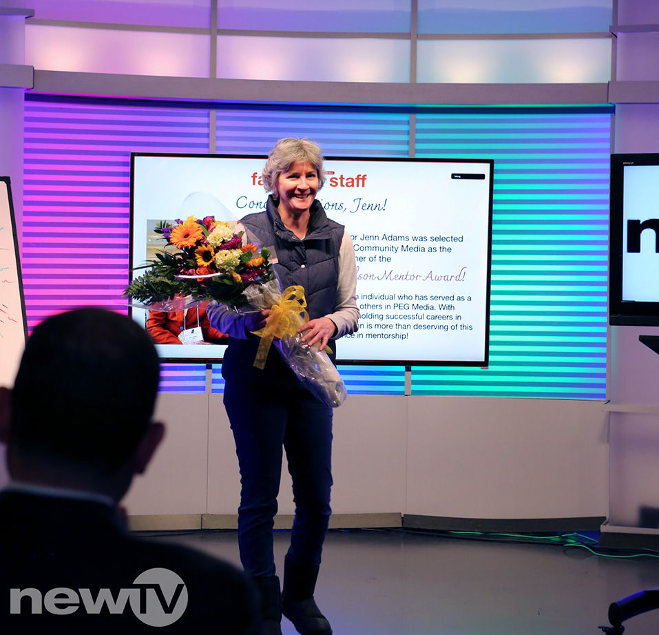 A woman standing in a television studio, holding a bouquet of flowers.