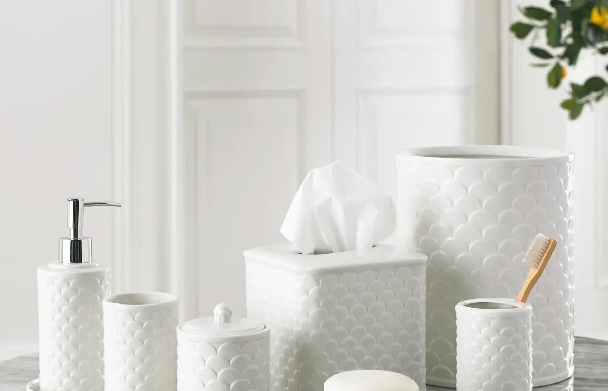 White textured bathroom accessories set on marble counter: soap pump, tissue box, canisters, cup, soap dish, and toothbrush holder.