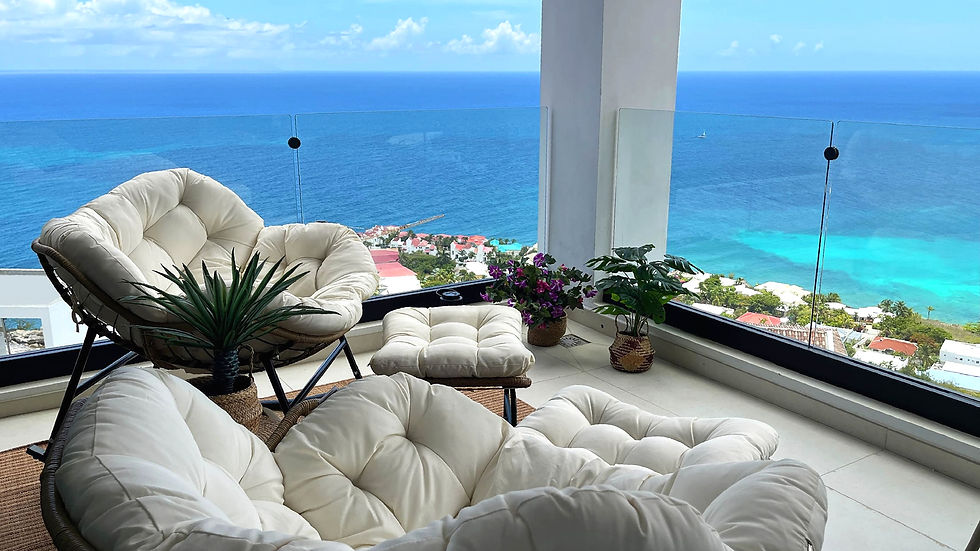 Coastal outdoor terrace with cream lounge chairs, tropical plants and panoramic Caribbean Sea views.