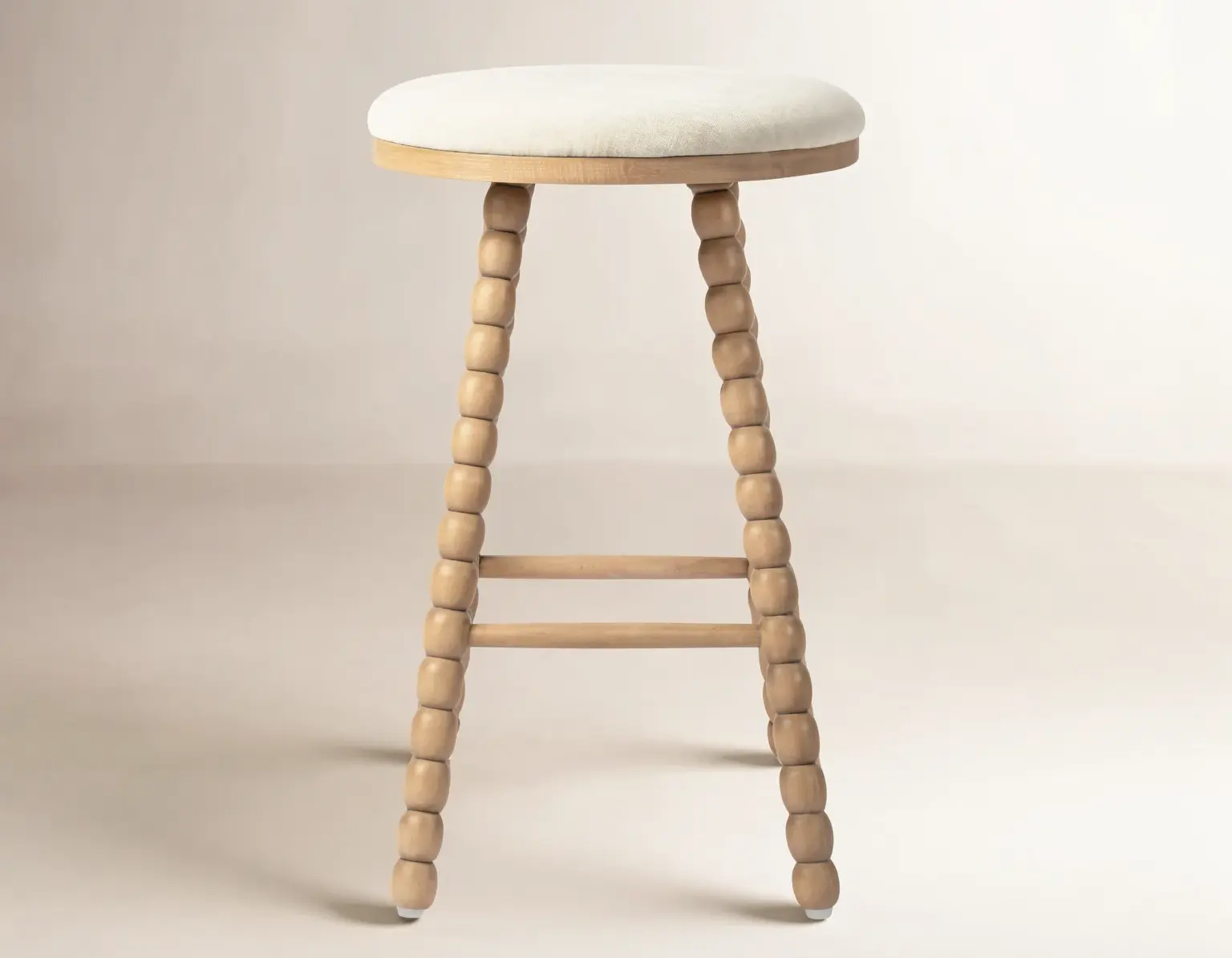 Minimal wooden stool with white cushioned seat on a soft beige studio backdrop