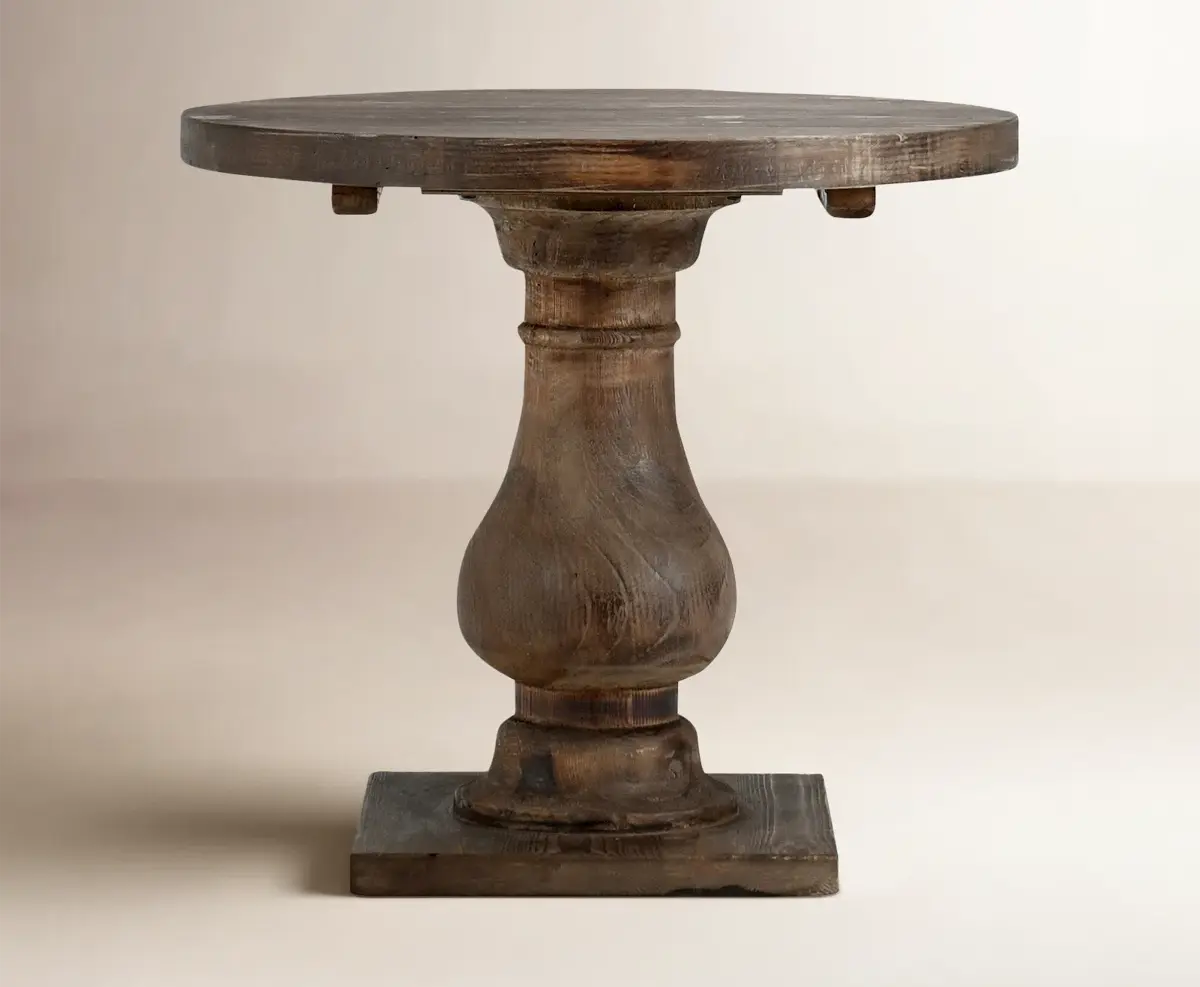 Rustic round wooden pedestal table on a plain beige backdrop, centered and isolated with no text.