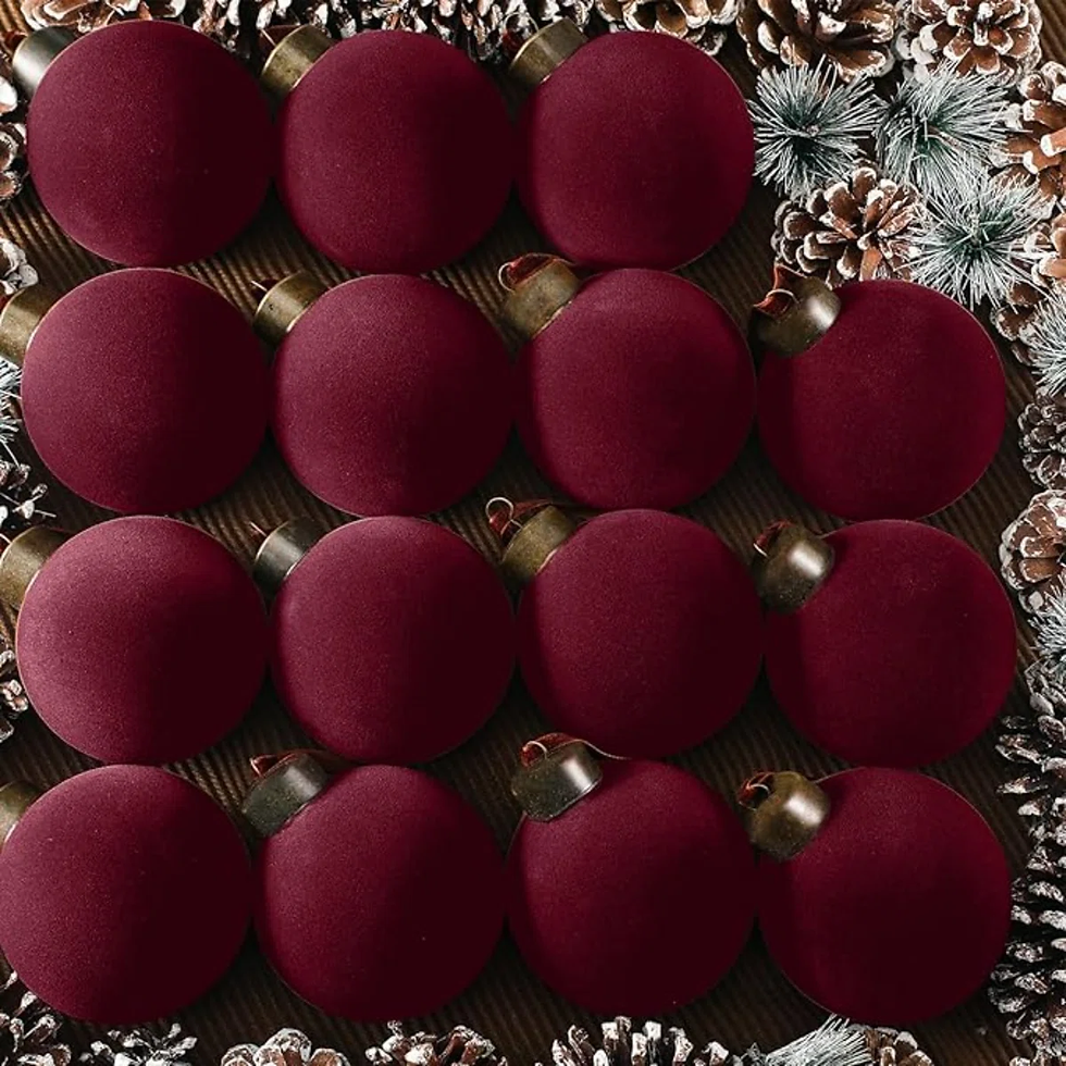 Burgundy velvet Christmas ornaments arranged in a grid, framed by frosted pine branches and pinecones on a rustic background.
