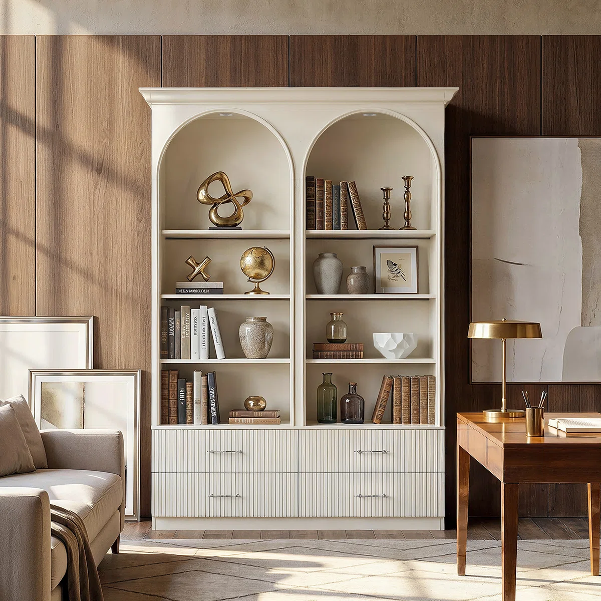 White arched bookcase with drawers, styled with books, pottery, and brass decor in a Nancy Meyers-inspired home office. Featuring classic millwork, warm wood paneling, and quiet luxury design, this timeless bookshelf creates an elegant and inviting traditional interior.