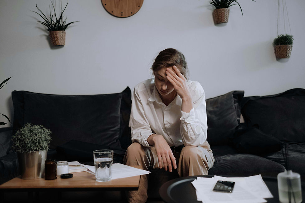 A stressed professional woman sits on her couch overwhelmed by paperwork, representing the need for online therapy in California or somatic therapy for stress in San Diego, CA with an online therapist.