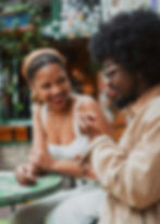 Smiling couple chatting at a cafe table outdoors, woman in white dress and headband, man in tan jacket | anxiety in relationships in Manhattan, NY | anxiety therapy | dating anxiety | Brooklyn Heights | West Village | Greenwich Village