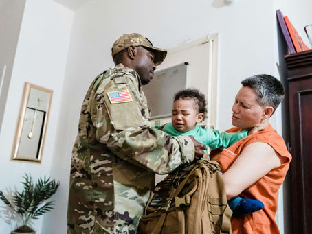 A man in military uniform, a woman holding a crying baby, and a tactical backpack, symbolizing the challenges addressed by a postpartum therapist and therapy for dads in Des Plaines, IL. Des Plaines, IL | Park Ridge, IL | Glenview, IL