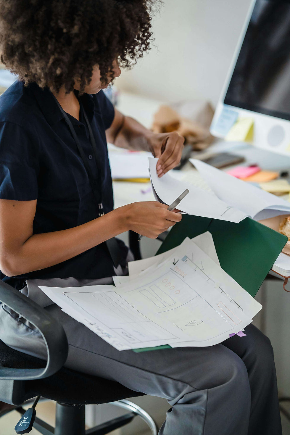 Woman with curly hair reviews and sketches paper design mockups at a desk beside a computer, focused and intent | therapist for anxiety | anxiety therapy for professionals | high functioning anxiety | Brooklyn Heights | West Village | Greenwich Village