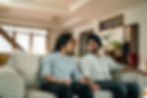 Happy South Asian couple sitting together on a sofa, holding hands and sharing a smile, reflecting emotional closeness fostered in South Asian couples therapy in NYC.