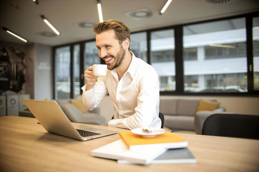 Man in a white shirt smiles while drinking coffee at a desk with a laptop and books | high functioning anxiety in Manhattan, NY | anxiety therapy | managing stress at work | Upper West Side | Upper East Side | Financial District