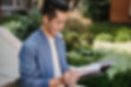 Smiling person in a blue jacket reads papers from a folder in a lush garden setting | anxiety therapy in Manhattan, NY | therapist for anxiety | high performing students | Midtown | Tribeca | Gramercy Park