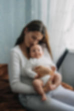 Image of a woman in white holding a baby, sitting on a bed | postpartum therapy in raleigh, nc | postpartum therapist in raleigh, nc | postpartum depression therapy | postpartum anxiety therapy | 27608 | 27610 | 28401