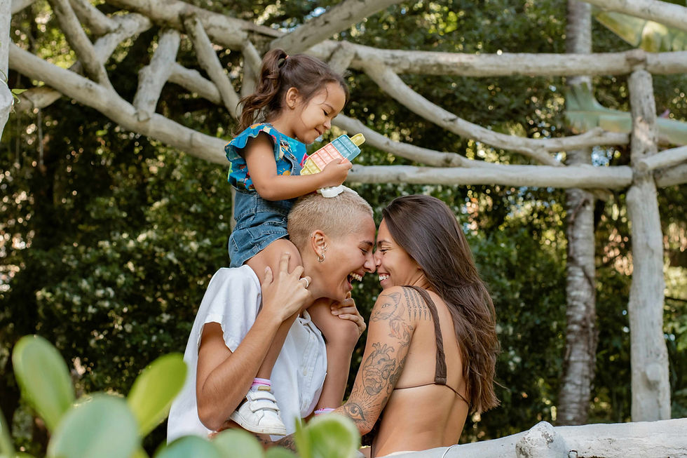 Two women laugh joyfully together outdoors with a child perched on one's shoulders, representing the chosen family connection and authentic belonging that becomes possible through healing. Somatic experiencing therapy in Golden, CO supports LGBTQ+ individuals and families in rebuilding trust and safety in their relationships after harm. Online therapy in Colorado makes this kind of affirming, body-centered care accessible to those who need it most, wherever they are.
