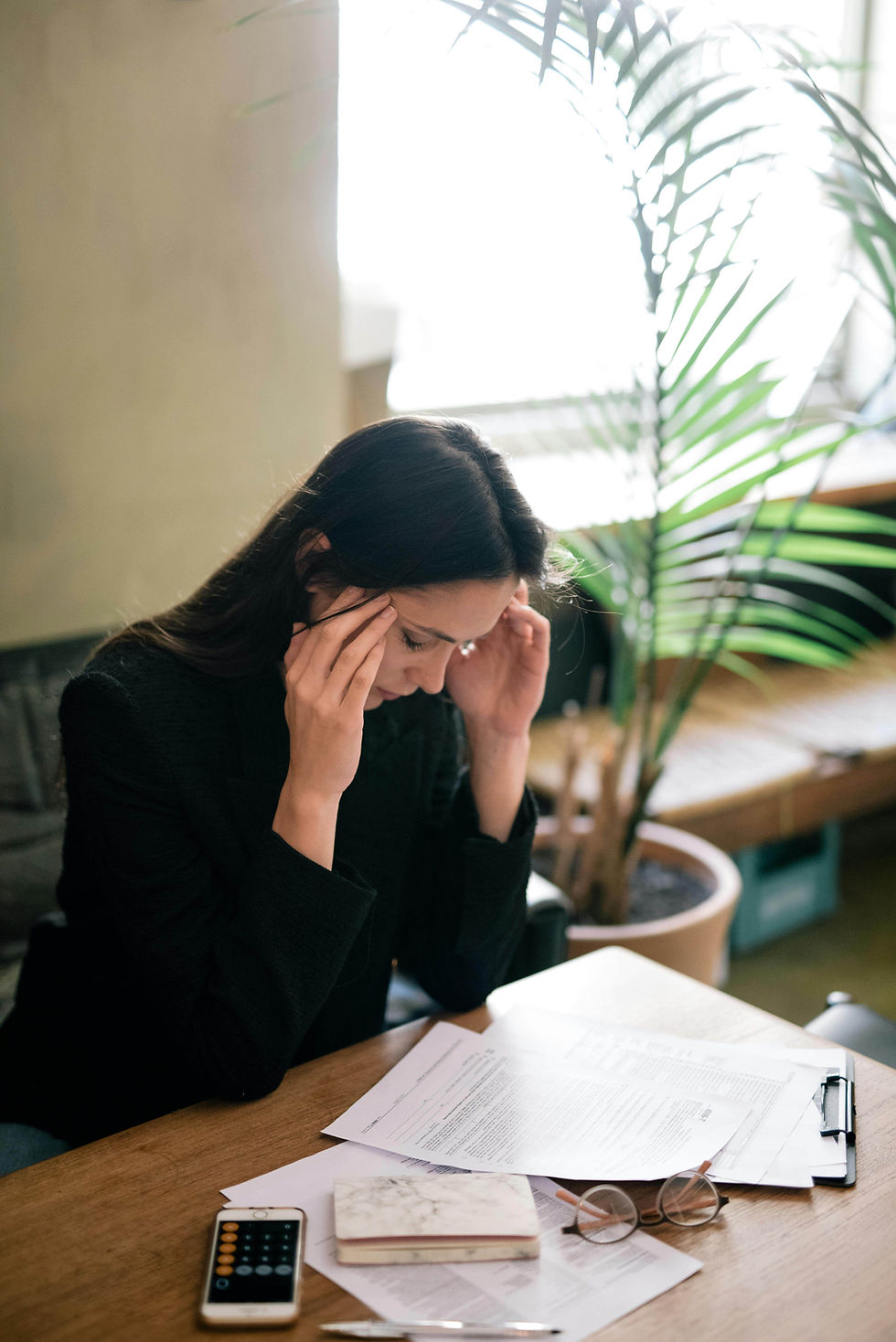 A woman sits at a desk with her head in her hands, surrounded by documents | therapist for anxiety in Manhattan, NY | anxiety therapy | high functioning anxiety | Upper West Side | Upper East Side | Financial District