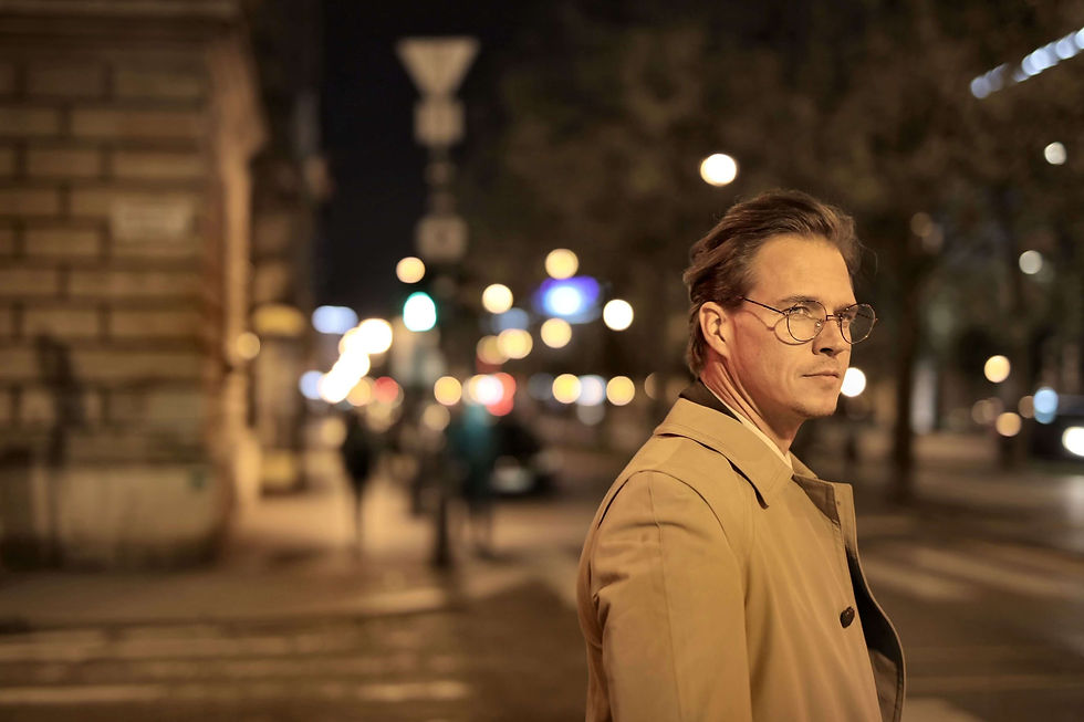 Man in a tan trench coat and glasses looks back on a city street at night, with blurred lights and pedestrians behind him | therapist for anxiety in Manhattan, NY | high functioning anxiety | anxiety therapy for professionals | Brooklyn Heights | West Village | Greenwich Village