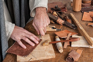 Leather artisan tools on a workbench with a craftsman's hands working on handmade leather goods.