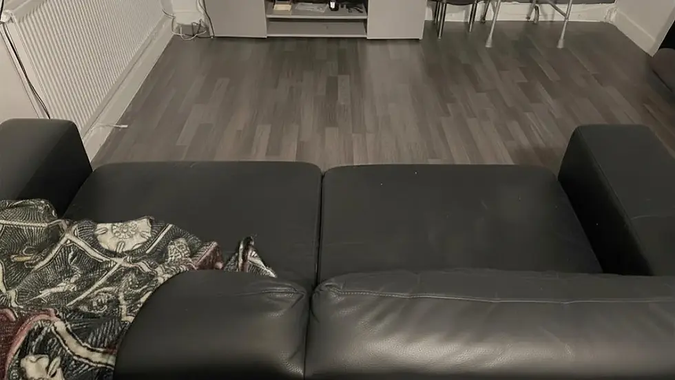 Black leather sofa with a patterned blanket on the armrest, in a room with a grey wooden floor