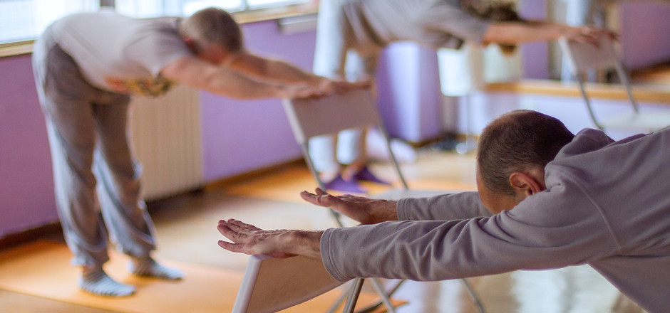 Yoga class, downward facing dog with the help of a chair done by three practitioners