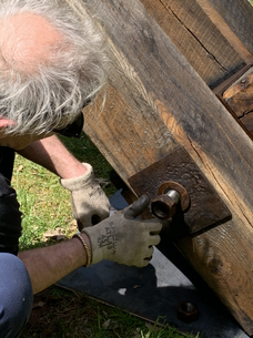 Man working on wood, using a wrench. Metal hardware visible. Outdoors.
