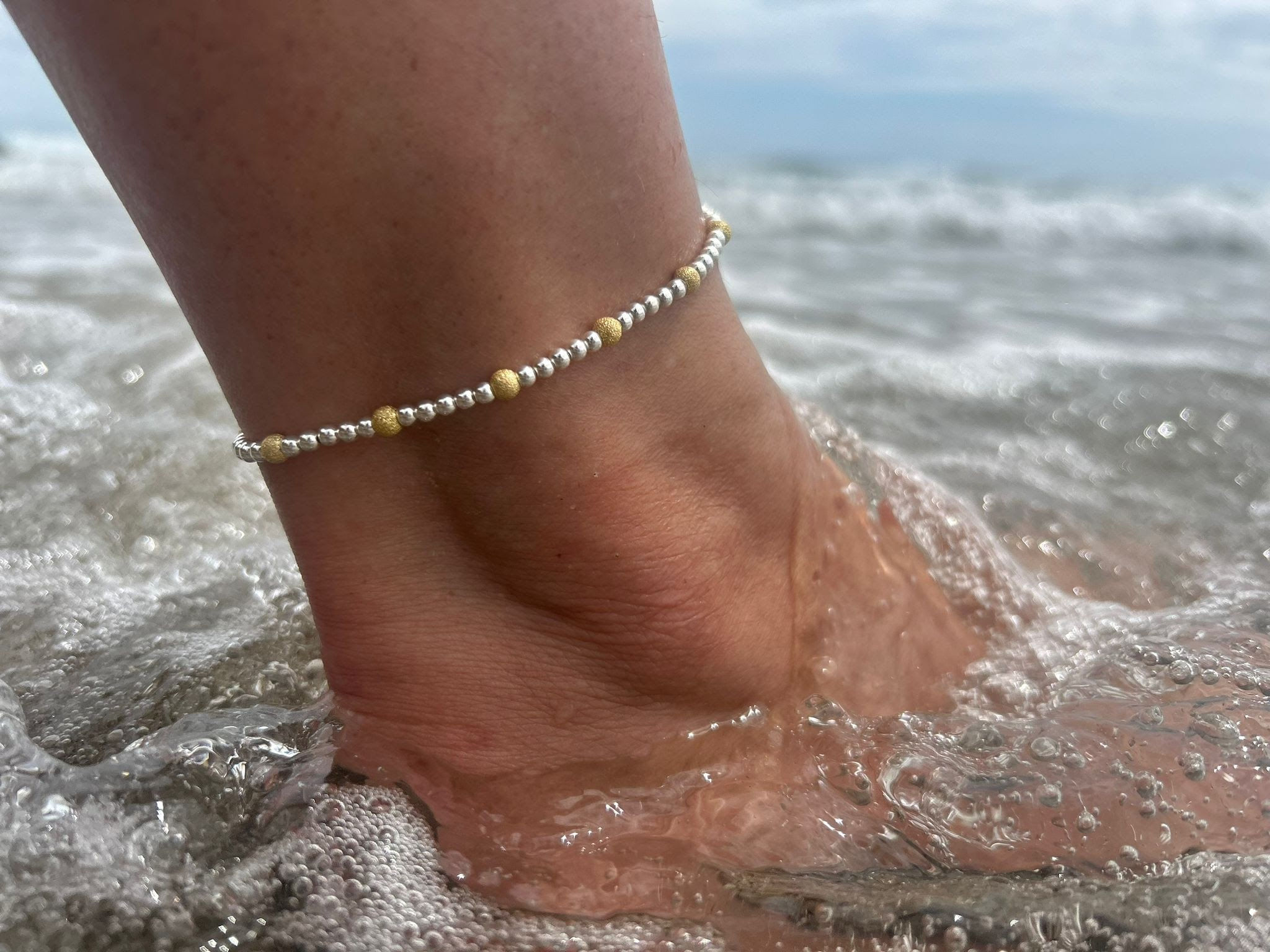 Model wearing a stretch sterling silver and gold effect frosted beaded anklet