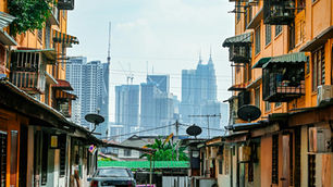 Contrast of old residential buildings in the foreground with modern city skyscrapers in the background, representing urban housing development and real estate growth.