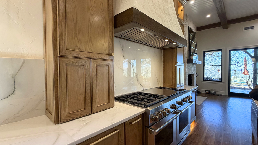 Professional gas range under a custom wood hood with full-height quartzite slab backsplash