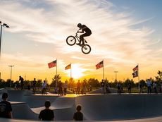 BMX rider launching a trick at Frisco Skate Park with red-white-and-blue bunting in the background at dusk