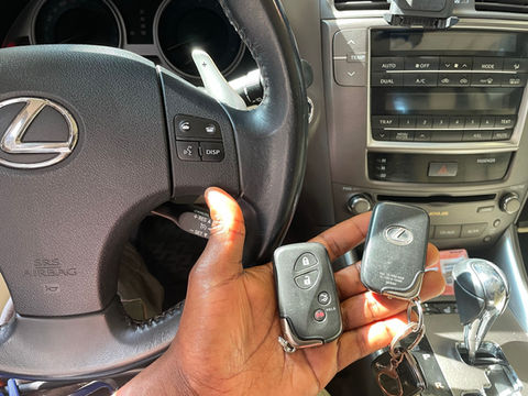 A person showing 2 keys in his hand while sitting inside a lexus
