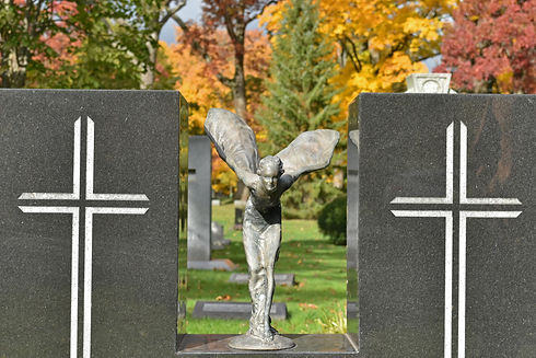 A bronze figure on a monument in a cemetery as autumn displays color in the background