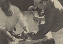 Two men working on a slab of stone using a hammer