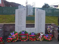 A memorial monument with several floral decorative pieces laid at the base of it