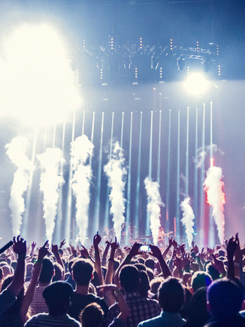Concert crowd with raised hands enjoying a music performance with bright lights.