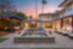 Twilight photo of a Spanish-style luxury home with a central pool, lounge seating, and pergola, captured by Ashley Blackmer P