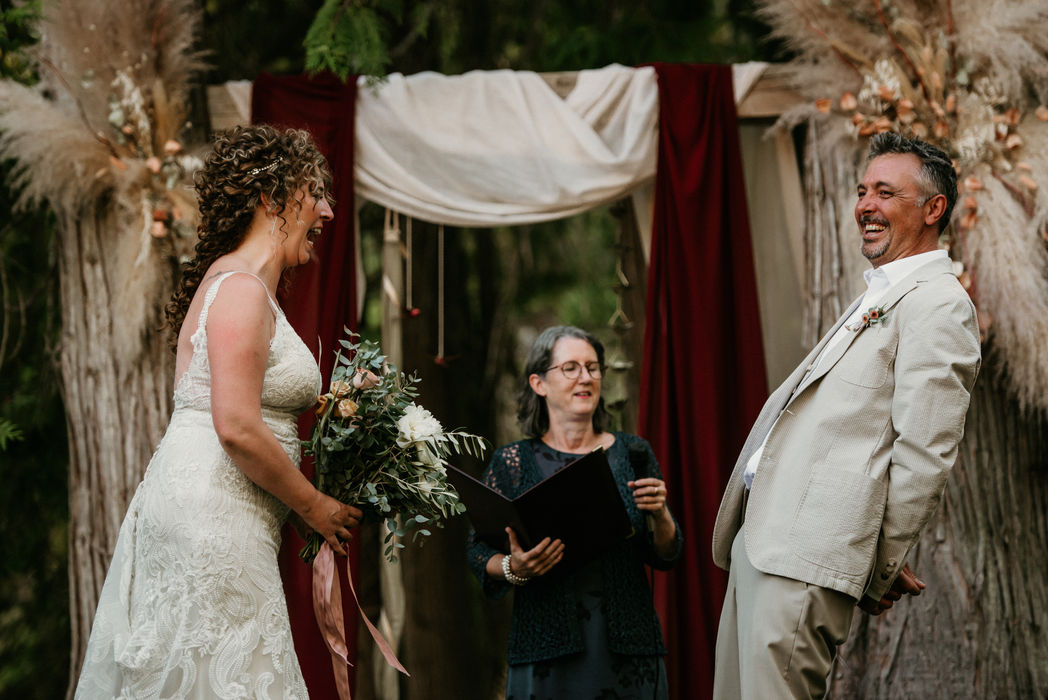 Bride & groom laughing during their outdoor wedding ceremony in the Shuswap, photographed by The Dark Room Studio.