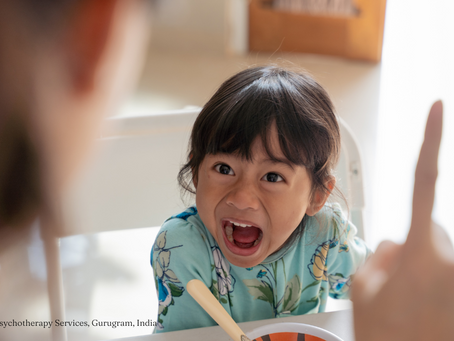 Angry child in floral blue shirt yelling at a parent, mid-meal — a visual example of emotional dysregulation in young children