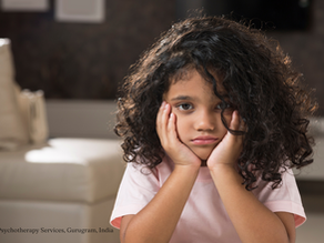 A curly-haired child sitting with her head in her hands, looking sad and withdrawn — capturing emotional heaviness and unspoken sadness.
