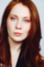 Lillee Jean Trueman official director and actress, in a professional portrait 2025. She is wearing a black blazer with her red hair side-parted, highlighting her fierce blue-green eyes.