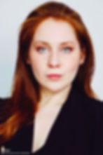 Lillee Jean Trueman official director and actress, in a professional portrait 2025. She is wearing a black blazer with her red hair side-parted, highlighting her fierce blue-green eyes.