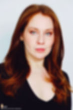 Lillee Jean Trueman official director and actress, in a professional portrait 2025. She is wearing a black blazer with her red hair side-parted, highlighting her fierce blue-green eyes.