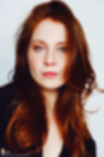 Lillee Jean Trueman official director and actress, in a professional portrait 2025. She is wearing a black blazer with her red hair side-parted, highlighting her fierce blue-green eyes.