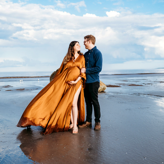 Photo of couples maternity photoshoot in the beach with mom to be wearing a flowy rust colored dress taken by Vanessa Keo photography in Salem, Ma