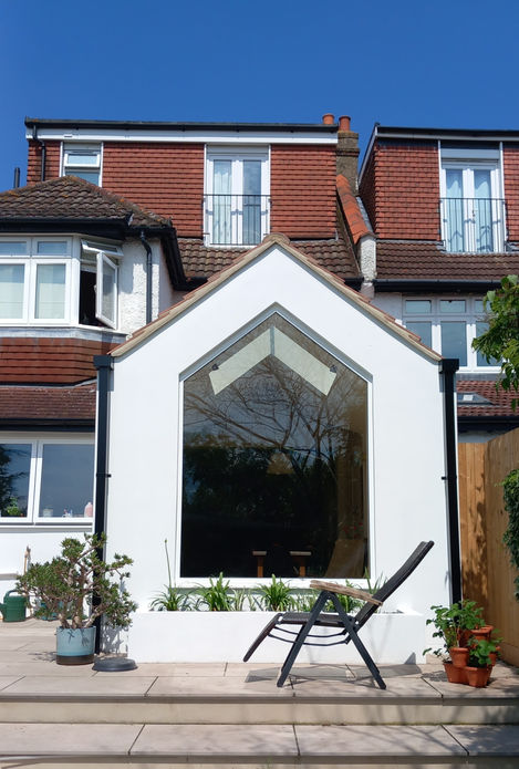 Rear extension from garden with apex window, replicated first-floor volume, and large planter with integrated greenery