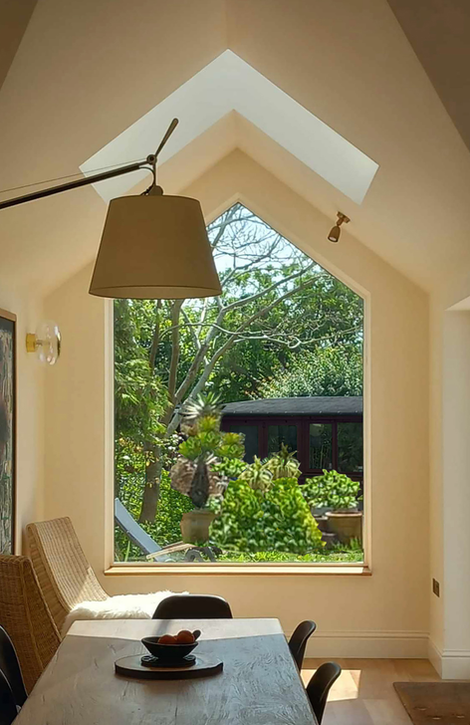 Edwardian extension with cathedral roof, ridge rooflight, apex window, dining area with oak table and wall light, rattan chairs, garden-like interior with botanical wallpaper and green armchairs