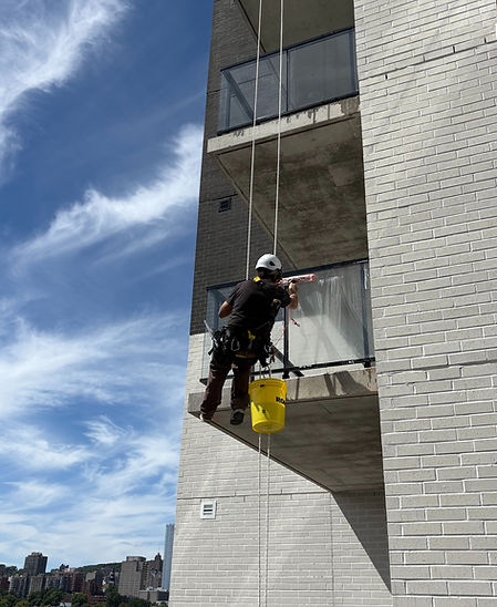 Rope access technician cleaning exterior windows on a commercial building in Montreal